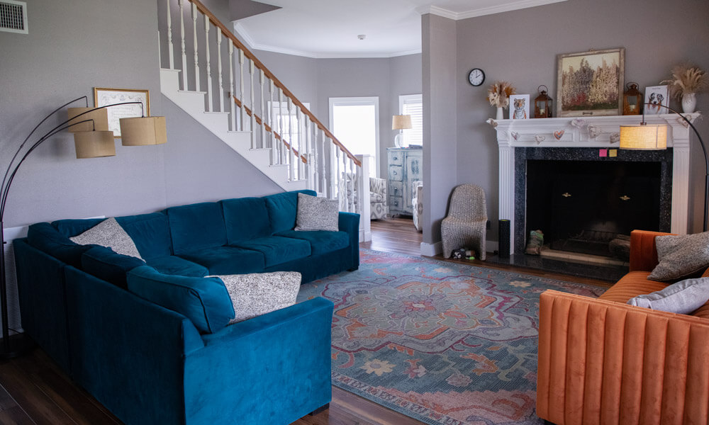 A cozy living room with modern, colorful furniture — including a teal sectional sofa and an orange armchair — arranged around a fireplace. The space feels inviting and comfortable, designed for group meetings or relaxation.