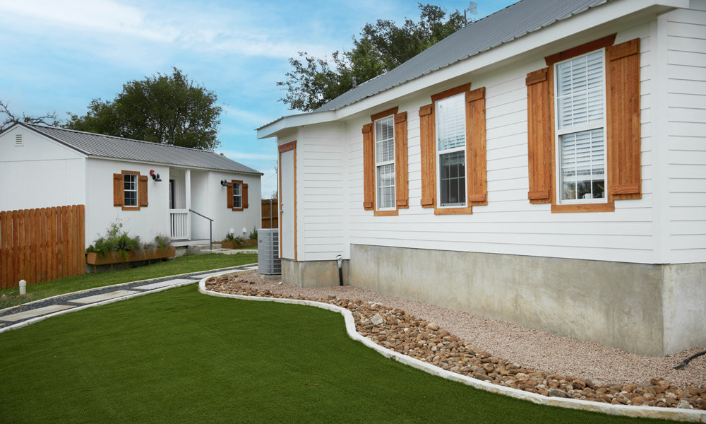 A peaceful outdoor setting featuring small white residential cottages with wooden shutters and a well-maintained lawn. The clean, structured pathways and serene environment evoke a sense of calm and order, ideal for a detox or recovery retreat.