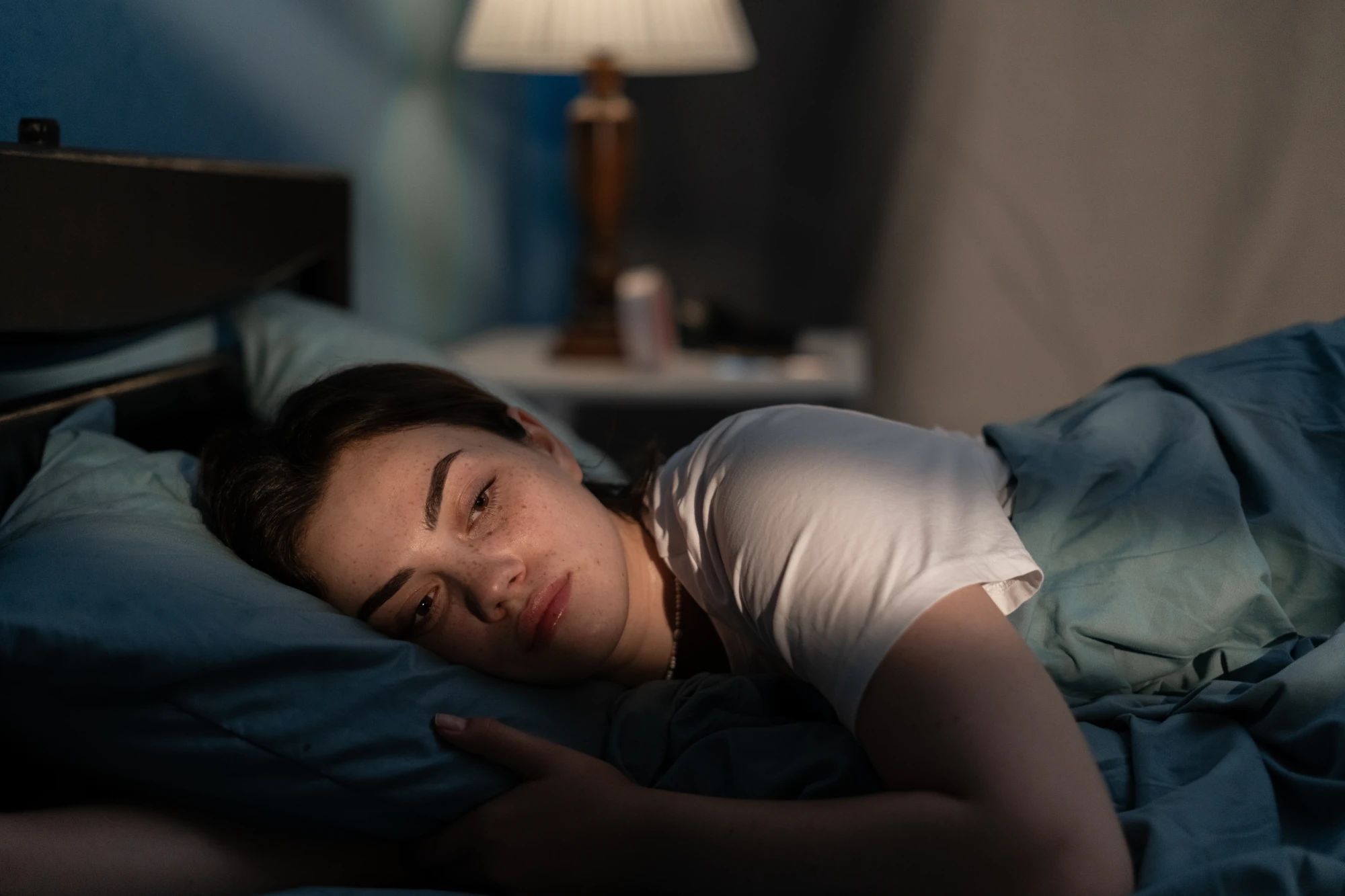 A woman lies awake in bed at night in a dimly lit bedroom.