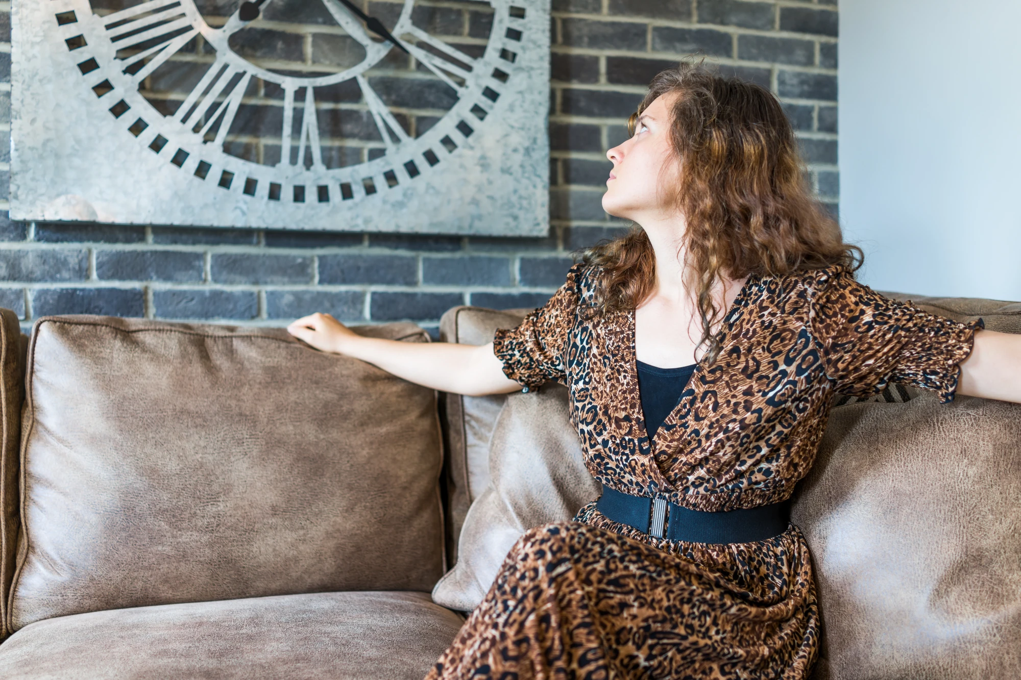 Woman sitting looking up at a wall clock with a thoughtful expression