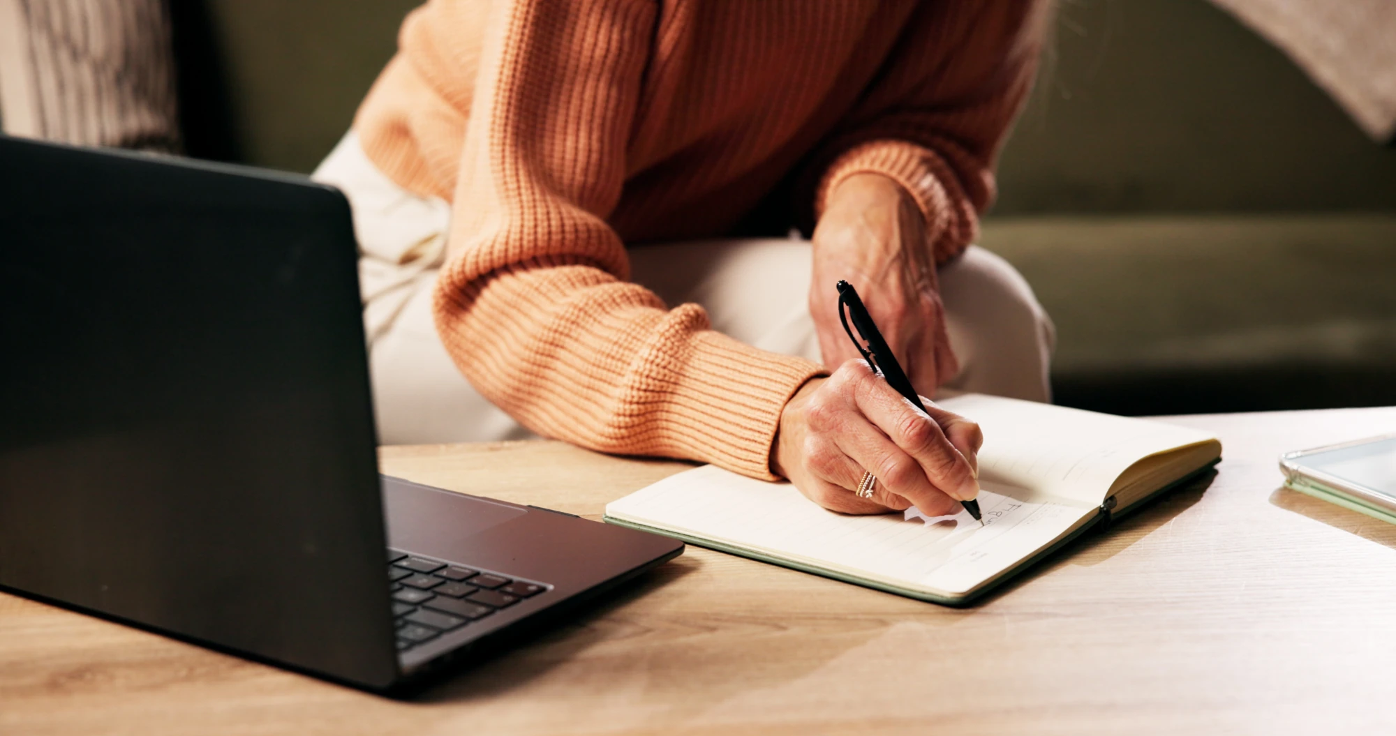 A woman writes in a notebook while sitting at a table at home
